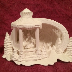 May include: White ceramic Christmas scene with a gazebo, trees, and a nativity scene inside. The gazebo has a snowy roof and icicle accents. The scene is perfect for painting and decorating.