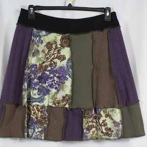 Könnte beinhalten: Ein Patchwork-Rock mit schwarzem Bund. Der Rock hat Bahnen aus lila, olivgrünem und braunem Stoff sowie Bahnen aus Stoff mit floralem Muster in Lila-, Grün- und Brauntönen. Der Rock hängt an einem schwarzen Kleiderbügel.