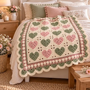 Könnte beinhalten: Eine gehäkelte Decke mit einem Gitter aus abwechselnden salbeigrünen und altrosa Herzmotiven auf cremefarbenem Grund. Die Decke ist mit einer gewellten Bordüre in Creme, Rosa und Salbeigrün versehen, die einen dekorativen Rand bildet.