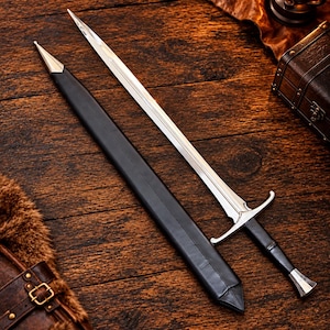 May include: A double-edged steel sword with a pointed tip, a silver crossguard, and a black leather-wrapped handle, accompanied by a matching black leather scabbard featuring a silver metal tip, presented as a complete set for display.