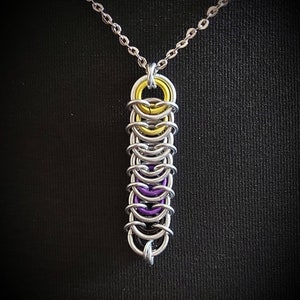 May include: A silver chain necklace with a pendant made of interlocking metal rings. The rings are coloured yellow and purple, creating a layered effect.