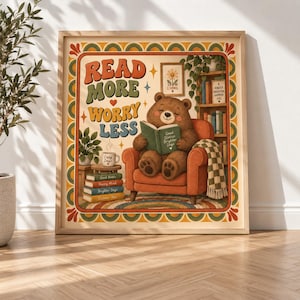 Puede incluir: Una lámina enmarcada con un oso pardo sentado en un sillón naranja leyendo un libro. El texto dice READ MORE WORRY LESS. La escena incluye una pila de libros, una planta en maceta y una estantería, todo enmarcado por un borde de estilo retro.
