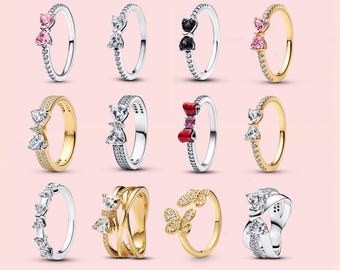 Könnte beinhalten: Eine Sammlung von zwölf Ringen in einem Raster angeordnet, mit verschiedenen Designs wie Schleifen und Schmetterlingen. Die Ringe bestehen aus silber- und goldfarbenem Metall und sind mit klaren, rosa, schwarzen und roten Steinen besetzt.