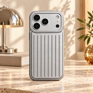 Op de afbeelding: Een zilverkleurige smartphonehoes met een verticale ribbeltextuur aan de onderkant en een gladde, verhoogde rechthoekige camerabehuizing aan de bovenkant. De hoes heeft een metallic afwerking en is ontworpen rond de drie cameralenzen.