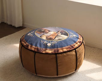 Può includere: Un pouf da pavimento rotondo con base in velluto color senape e profili neri. La superficie superiore è blu e mostra una stampa di un dipinto classico raffigurante una persona che suona il liuto, incorniciata da un bordo decorativo floreale.