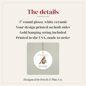 May include: A 7.62 cm round glossy white ceramic ornament featuring a brown thrasher bird illustration on a branch with red berries. The text reads Georgia, Brown Thrasher, and Christmas 2026. A gold hanging string is attached to the top of the ornament.