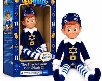 May include: A plush elf doll named Geltie with brown hair, pointed ears, and a blue velvet outfit featuring a yellow Star of David, white faux fur trim, and blue and white striped legs. The doll is displayed next to its blue branded packaging.