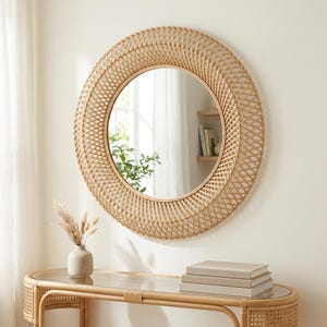 May include: A round wall mirror featuring a wide, intricate frame made of woven light brown rattan. The frame has a crisscross lattice pattern that surrounds the circular glass center, creating a textured, layered appearance.