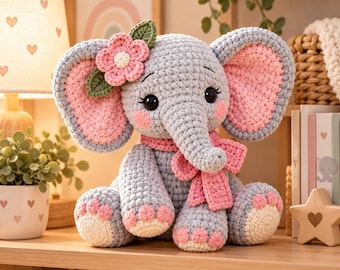 Könnte beinhalten: Ein graues, gehäkeltes Elefanten-Stofftier mit großen Ohren mit rosa Innenseiten, einem rosa gehäkelten Schal und einer rosa Blume mit grünen Blättern am Kopf. Der Elefant hat schwarze Augen, rosa Wangen und cremefarbene Akzente an den Füßen.