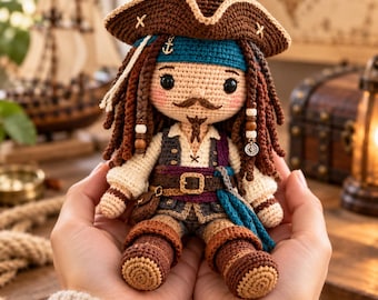 Könnte beinhalten: Eine gehäkelte Piratenpuppe mit braunem Dreispitz, langem dunkelbraunem Garnhaar mit Perlen, einem blaugrünen Stirnband, weißem Hemd, dunkler Weste, braunem Gürtel mit Schnalle und braunen Stiefeln. Die Puppe hat schwarze Augen und einen gestickten Schnurrbart.