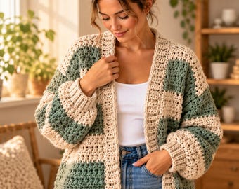 Könnte beinhalten: Eine grob gehäkelte Strickjacke mit einem Color-Block-Muster aus abwechselnden cremefarbenen und salbeigrünen rechteckigen Feldern. Das Kleidungsstück hat lange Ärmel mit gerippten Bündchen, einen gerippten Saum und eine offene Vorderseite.