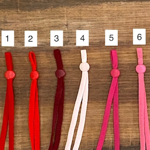 May include: Six different colors of elastic cord with metal tips. The colors are red, burgundy, pink, light pink, and two shades of pink. The cords are numbered 1 through 6.