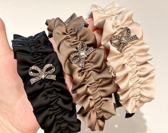 Diadema de satén con volantes y lazo de pedrería, elegante accesorio para el cabello plisado.
