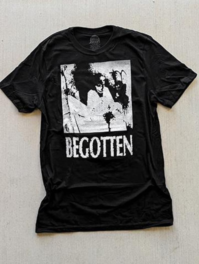 May include: A black short-sleeve t-shirt featuring a white rectangular graphic print on the chest. The graphic depicts a high-contrast, grainy scene with the word BEGOTTEN printed in a distressed, bold white font directly below the image.