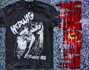 May include: A black short-sleeve t-shirt featuring a white graphic print of a person singing with the text Hedwig and the Angry Inch. The design includes additional text layered over the figure and a vertical red dripping text element.