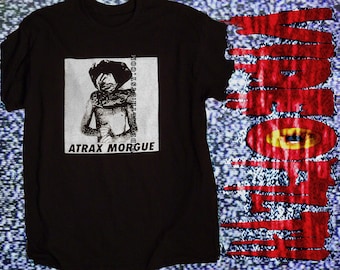 May include: A black t-shirt featuring a white square graphic on the chest with a black and white illustration of a figure and the text ATRAX MORGUE. To the right, a large red vertical graphic with a yellow eye design and dripping text.