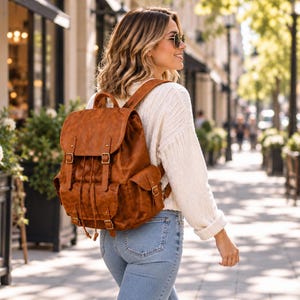 May include: A tan brown backpack featuring a fold-over flap with two buckle straps, a drawstring closure, and two side pockets. The bag is constructed with a textured finish and includes a top handle and adjustable shoulder straps.