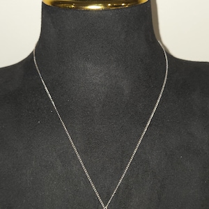 May include: A silver-toned chain necklace featuring a single round, cream-coloured pearl pendant. The set includes a pair of matching round, cream-coloured pearl stud earrings. The jewellery is displayed on a black neck form with a gold-toned collar.