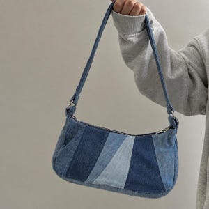 Peut inclure: Un petit sac à bandoulière fabriqué en tissu denim patchwork dans des nuances de bleu variées. Le sac présente une forme rectangulaire aux coins arrondis, une sangle unique fixée par des anneaux en métal argenté et une fermeture éclair.