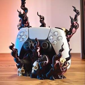 Könnte beinhalten: Ein weißer Videospiel-Controller in einem dekorativen Ständer, der mit dunkelvioletten, flammenartigen Strukturen und mehreren kleinen, cremeweißen menschlichen Schädeln verziert ist, die in die Basis integriert sind.