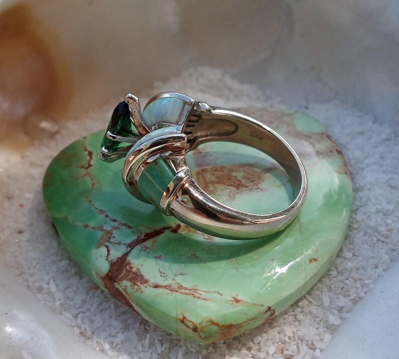 May include: A silver ring with a green gemstone, a white opal, and a green stone set in a silver band.