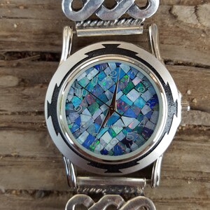 May include: A silver watch with a blue and white opal mosaic face and a silver Celtic knot band.