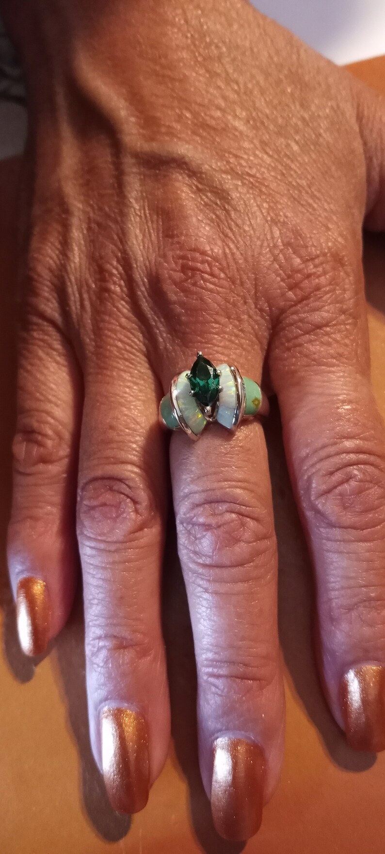 May include: A silver ring with a green gemstone and white opal accents. The ring is on a person's finger.