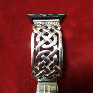May include: Silver watch band with a Celtic knot design. The band is made of metal and has a polished finish.