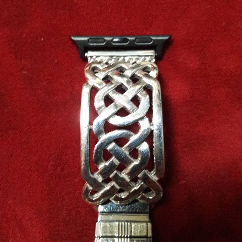 May include: Silver watch band with a Celtic knot design. The band is made of metal and has a polished finish.