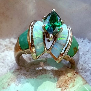 May include: A silver ring with a green gemstone surrounded by white opal and green turquoise stones.