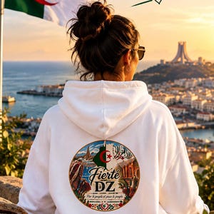 Peut inclure: Un sweat-shirt à capuche blanc avec un motif circulaire au dos. Le design inclut le drapeau algérien, des monuments architecturaux et le texte Fierte DZ, Par le peuple et pour le peuple, avec un cœur et des bordures décoratives.