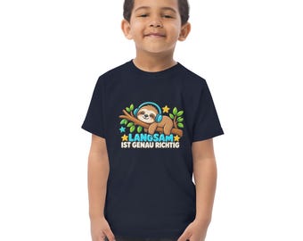 Könnte beinhalten: Ein dunkelblaues Kurzarm-T-Shirt mit einer Grafik eines braunen Faultiers, das blaue Kopfhörer trägt und auf einem Ast liegt. Das Design enthält grüne Blätter, gelbe und blaue Sterne sowie den weißen Schriftzug "LANGSAM IST GENAU RICHTIG".