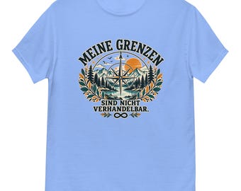 Könnte beinhalten: Ein hellblaues T-Shirt mit einem Grafikdruck, der einen Kompass, Berge, Tannen und einen Sonnenuntergang zeigt. Der Text lautet "MEINE GRENZEN SIND NICHT VERHANDELBAR." mit einem Unendlichkeitssymbol, umgeben von dekorativen Blättern.