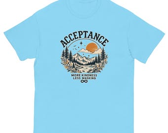 Könnte beinhalten: Ein hellblaues T-Shirt mit kurzen Ärmeln und einer kreisförmigen Grafik einer Berglandschaft mit Tannen, einer Sonne und Sternen. Der Text lautet "ACCEPTANCE" oben und "MORE KINDNESS LESS MASKING" unten mit einem Unendlichkeitssymbol.