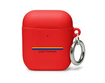 Könnte beinhalten: Eine leuchtend rote Silikon-Schutzhülle für kabellose Ohrhörer mit einem horizontalen Regenbogenstreifen-Motiv über dem schwarzen Schriftzug "just human", der mittig auf der Vorderseite platziert ist. Ein silberner, runder Karabinerhaken ist seitlich befestigt.