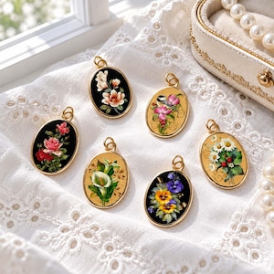 May include: Six oval-shaped metal pendants featuring detailed floral illustrations. Three pendants have black backgrounds with roses, lilies, and pansies, while three have gold-toned backgrounds with daisies, calla lilies, and a bird.