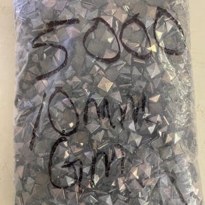 May include: A clear plastic bag filled with numerous small, gray, pyramid-shaped objects. The bag has handwritten text that reads "5000 10mm Gm". The objects appear to be reflective and metallic.