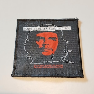 May include: A square black fabric patch featuring a red embroidered portrait of Che Guevara outlined in white. The text RAGE AGAINST THE MACHINE appears in white at the top, with 1994 RAGE AGAINST THE MACHINE THE GIANT MERCHANDISE COLLECTION in red below.