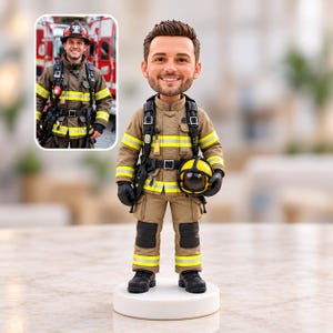 May include: A custom bobblehead figurine of a firefighter wearing a tan turnout coat with yellow reflective stripes, black gloves, and black boots. The figure holds a yellow helmet and features a detailed head sculpt with brown hair.