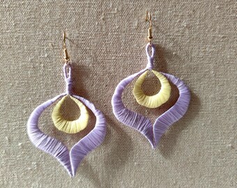 Può includere: Un paio di orecchini pendenti color lavanda e giallo con un design astratto unico. Gli orecchini sono realizzati con fili sottili e intrecciati e hanno un aspetto delicato e femminile.