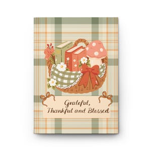 Puede incluir: Una tarjeta rectangular con un fondo de cuadros verdes y naranjas. En el centro, una cesta tejida contiene dos libros, un hongo y flores, decorada con una tela de cuadros verdes y un lazo rojo. El texto dice: Grateful, Thankful and Blessed.