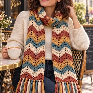 May include: A long crochet scarf featuring a chevron pattern in alternating stripes of rust orange, mustard yellow, cream, and teal blue. The scarf is finished with long, multi-colored fringe tassels at both ends, incorporating all four colors.