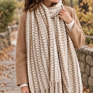 May include: A long, rectangular crochet scarf featuring a textured, repeating bobble stitch pattern in alternating shades of cream, beige, and light brown. The scarf is finished with long, straight fringe tassels along both bottom edges.