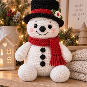 Peut inclure: Une poupée bonhomme de neige crochetée en blanc avec un haut-de-forme noir orné d'une bande rouge et d'une petite fleur, une écharpe rouge à franges et trois boutons noirs sur le torse. Il a des joues roses, des yeux noirs et un sourire brodé.