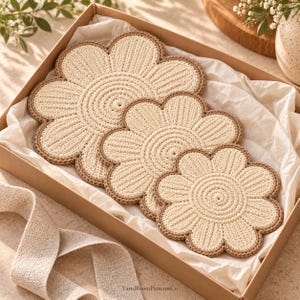 May include: Three cream-colored, flower-shaped crochet coasters with brown edges, arranged in a cardboard gift box lined with white tissue paper. The text YarnBloomPatternsCo is printed at the bottom of the box.