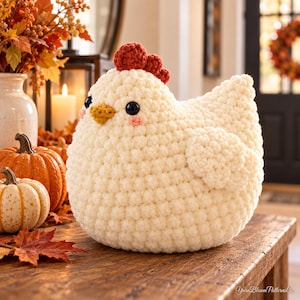 May include: A cream-colored crochet chicken plush toy featuring a textured yarn body, a dark red comb, a small yellow beak, and black bead eyes with pink blush accents. The text YarnBloomPatternsCo is visible in the bottom right corner of the image.