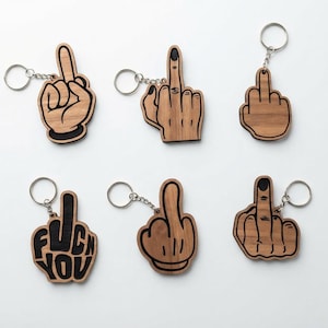 May include: Six wooden keychains featuring hand gestures of a middle finger raised in a defiant pose. The designs include various hand styles, some with black painted details, and one keychain clearly displaying the text FUCK YOU in black.