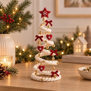 Puede incluir: Una decoración de árbol de Navidad en espiral hecha de cuerda trenzada blanca gruesa. El árbol está adornado con pequeños adornos esféricos dorados, lazos de tela roja y adornos rojos en forma de corazón. Una estrella roja con un copo blanco corona la punta.