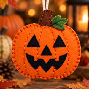 May include: A felt jack-o'-lantern ornament in bright orange with a brown stem and a green leaf. The pumpkin features black felt triangular eyes, a triangular nose, and a jagged mouth, all stitched with orange thread and hanging from a white cord.
