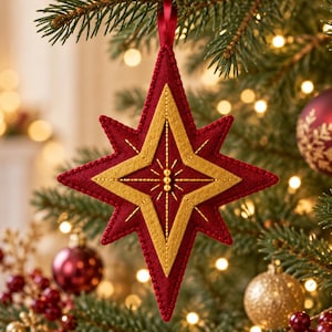 May include: A star-shaped Christmas ornament made of layered felt in deep red and gold. The ornament features intricate gold embroidery, a central vertical line of small gold beads, and a red ribbon loop for hanging on a tree branch.
